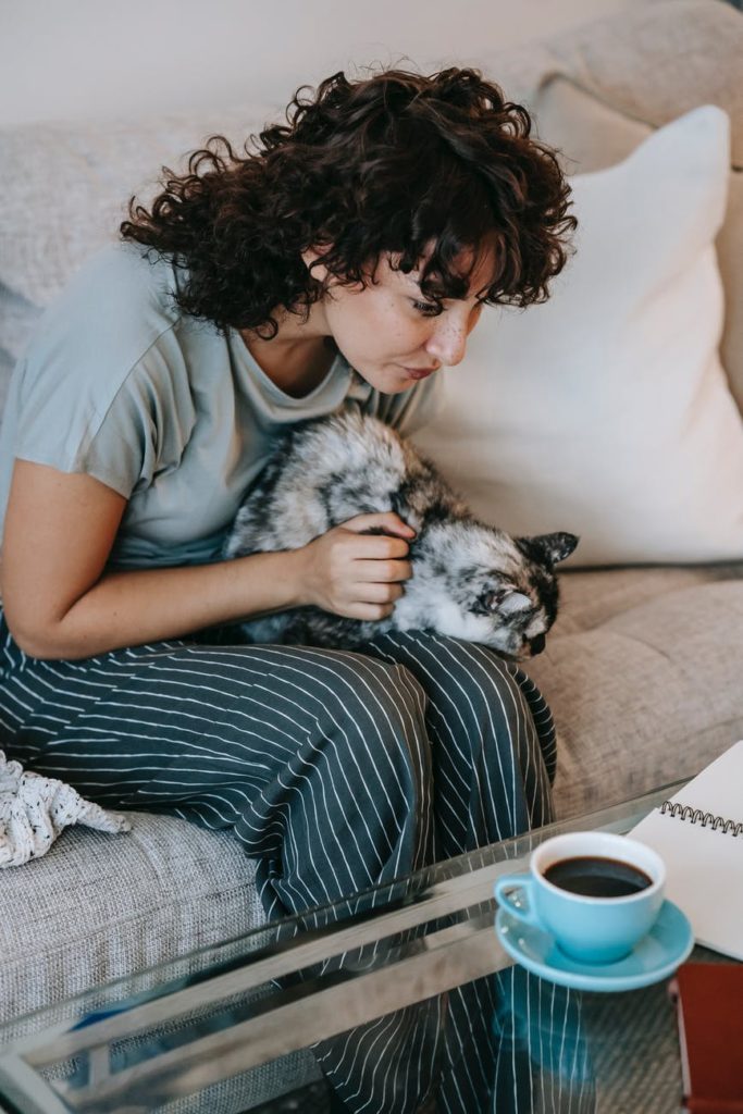 young woman with curly hair in striped trousers patting cat